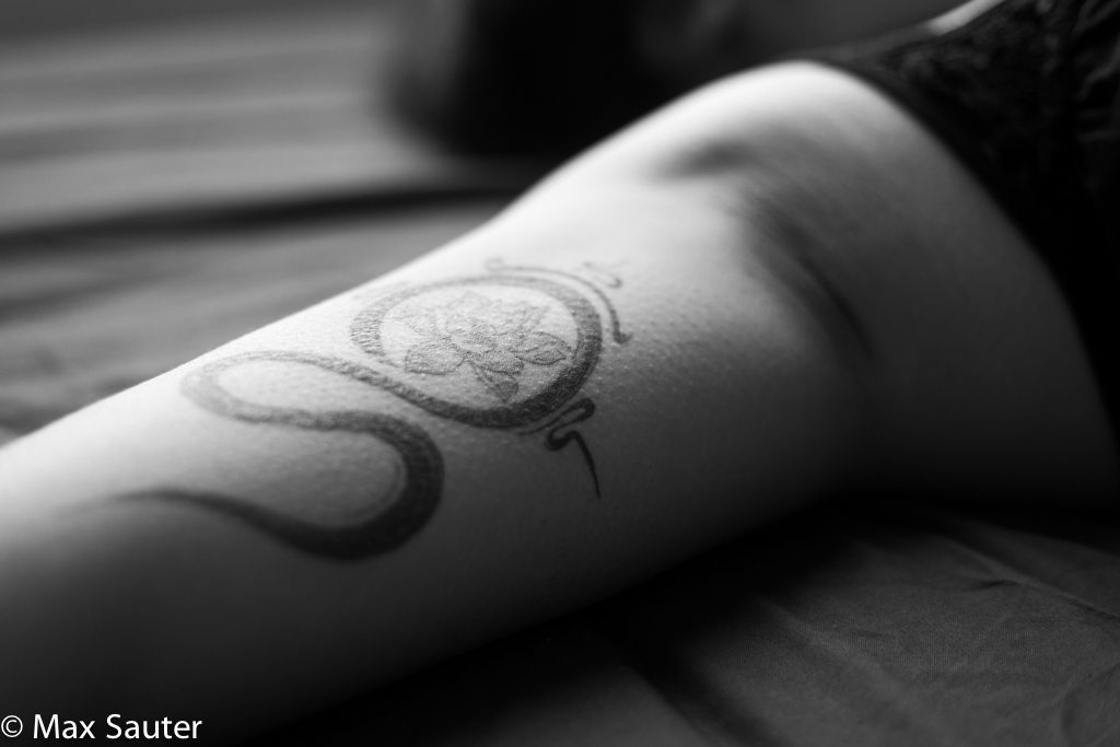 modèle allongée sur le lit, focus sur le tatouage situé sur le bras